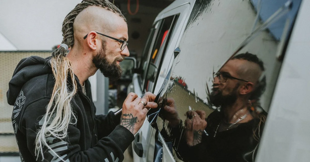 Homme appliquant un autocollant sur une voiture, reflétant créativité et style.
