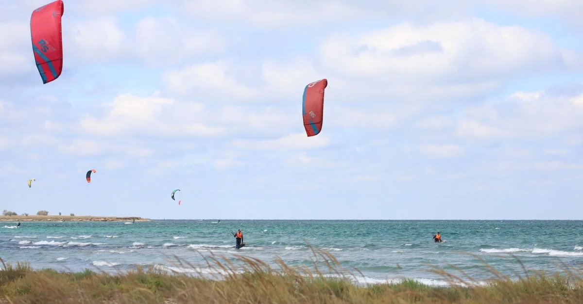 Kitesurfeurs profitant d'une journée ensoleillée et venteuse sur l'océan avec des cerfs-volants colorés s'élevant haut dans le ciel.