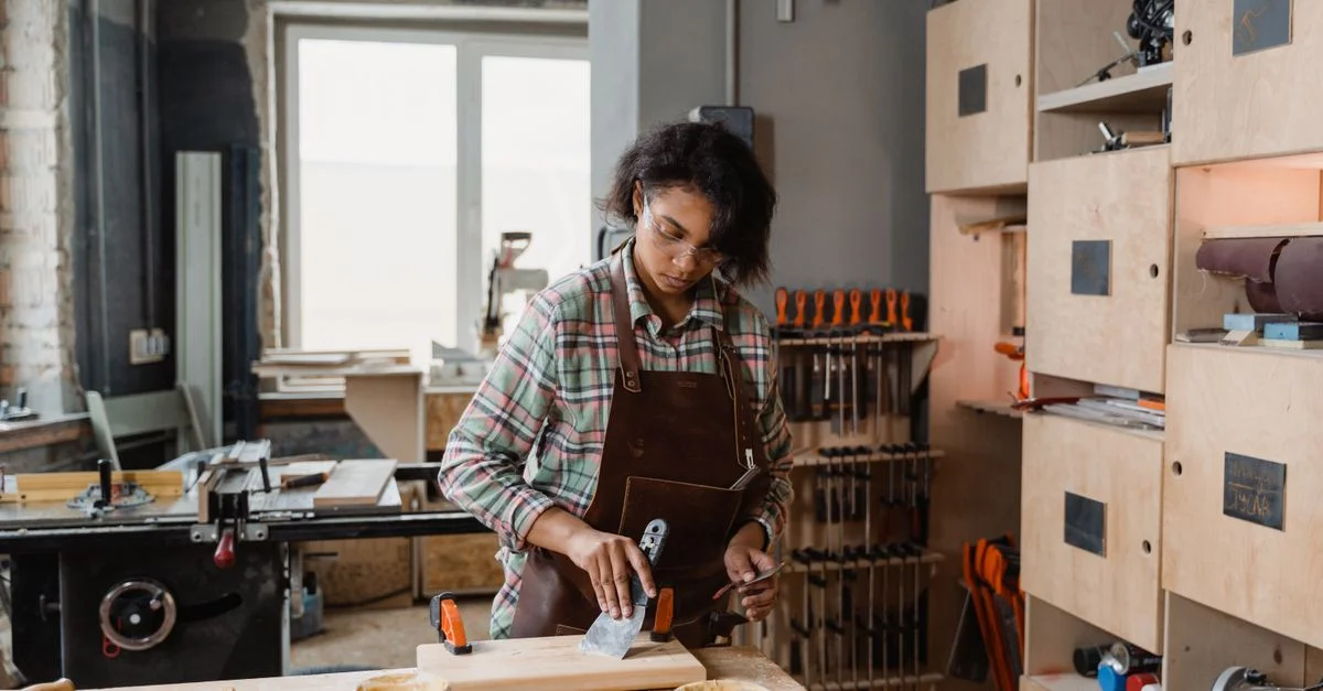 Femme utilisant des outils à main dans un atelier de menuiserie cosy, façonnant des pièces en bois avec compétence.