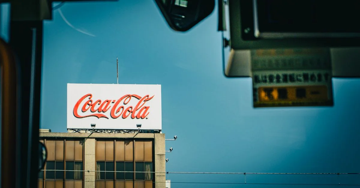 Panneau Coca Cola sur un bâtiment sous un ciel bleu clair, vu de l'intérieur.