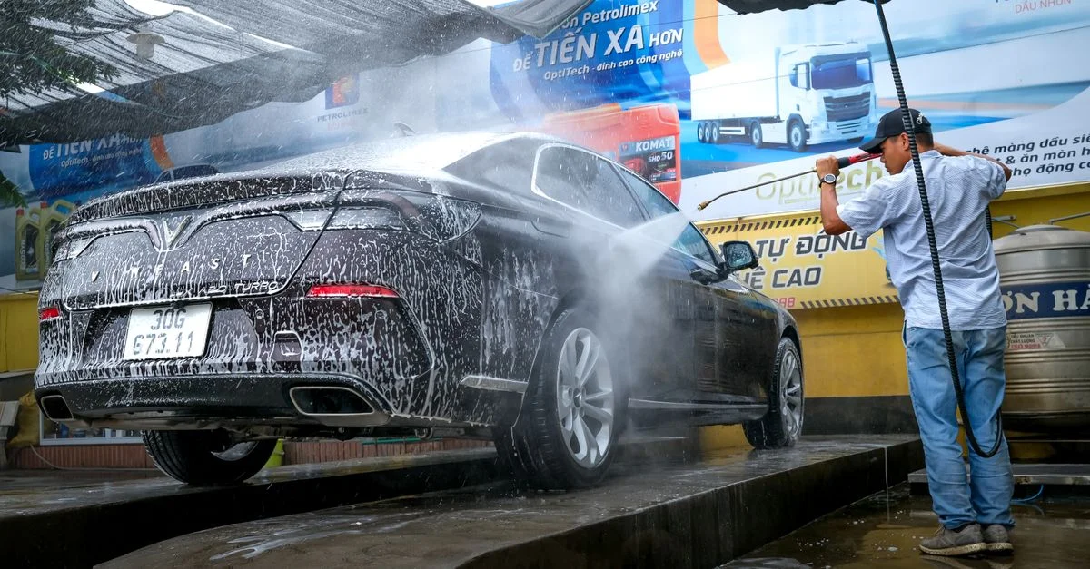 Une voiture noire est nettoyée avec un pulvérisateur à haute pression par un homme dans une station de lavage de voiture en extérieur.