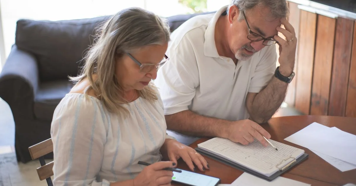 Couple âgé examinant des factures et des documents à la maison, se concentrant sur les finances et la technologie.