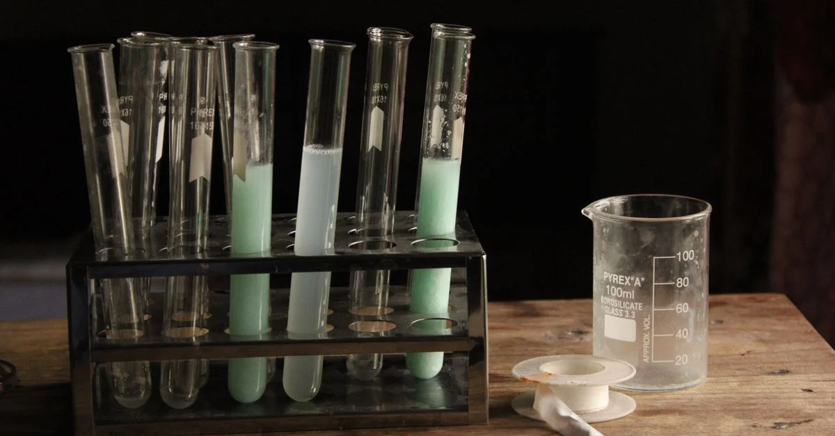 Tubes à essai et bécher contenant des produits chimiques colorés sur une table en bois dans un laboratoire faiblement éclairé.