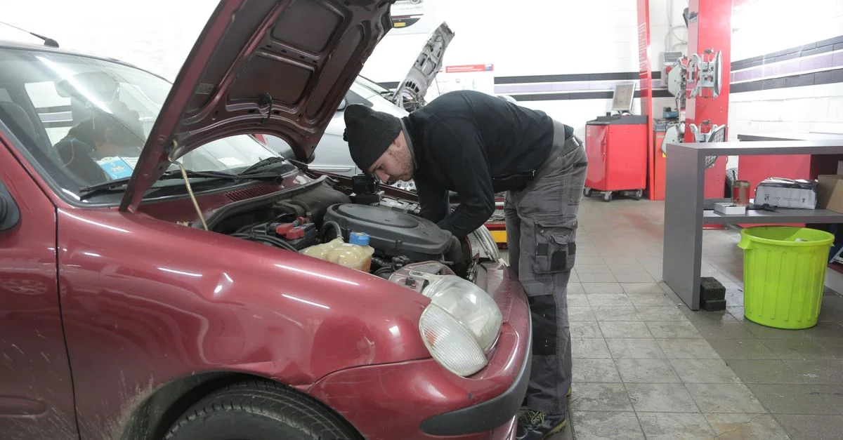 Un mécanicien effectue une inspection du moteur sur une voiture rouge à l'intérieur, dans un atelier de garage.